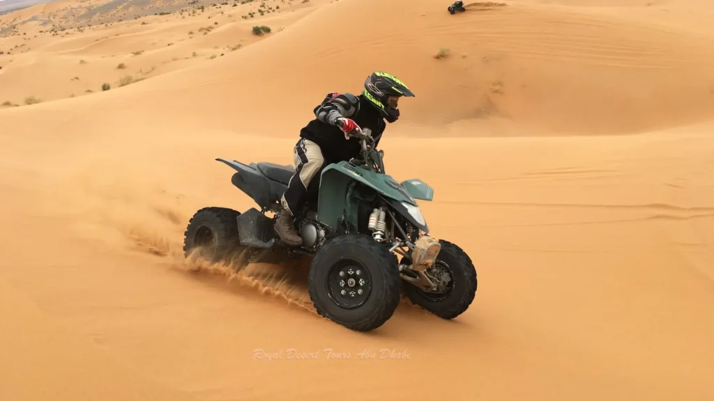 Tourist riding a quad bike over desert dunes during a morning desert safari in Abu Dhabi.